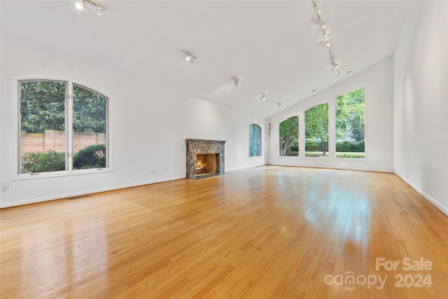 unfurnished living room with a high end fireplace, light hardwood / wood-style floors, vaulted ceiling, and plenty of natural light