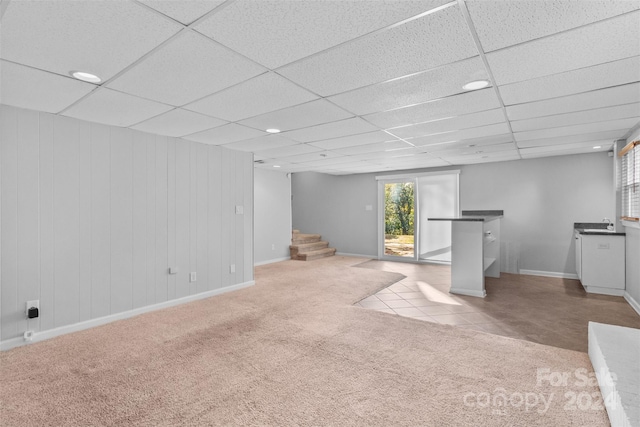 basement featuring a paneled ceiling, wood walls, and light colored carpet