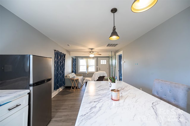 kitchen with stainless steel refrigerator, white cabinetry, hanging light fixtures, light stone counters, and dark hardwood / wood-style flooring