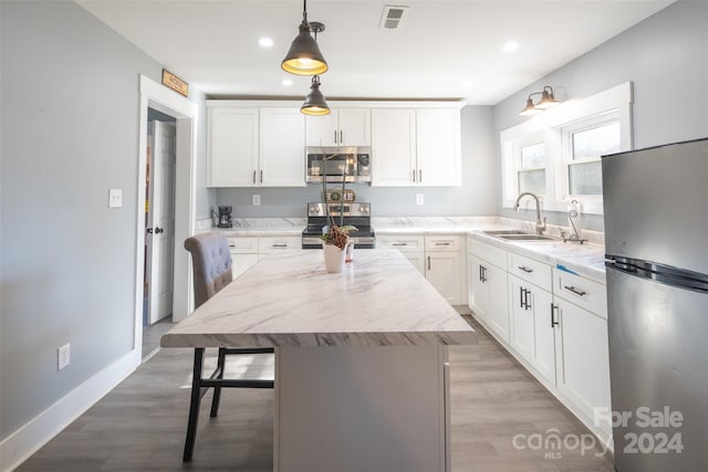 kitchen featuring white cabinets, a center island, stainless steel appliances, and hanging light fixtures