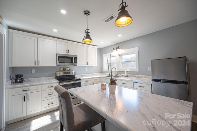 kitchen with white cabinets, a kitchen bar, appliances with stainless steel finishes, and light hardwood / wood-style flooring