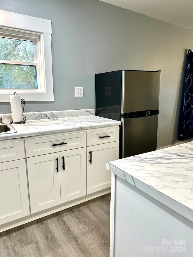 kitchen with white cabinets, light hardwood / wood-style flooring, stainless steel refrigerator, and sink