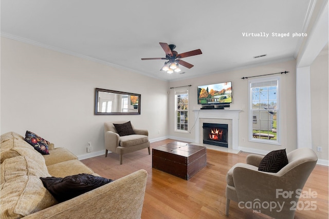 living room with a fireplace with flush hearth, a ceiling fan, baseboards, light wood-style floors, and ornamental molding