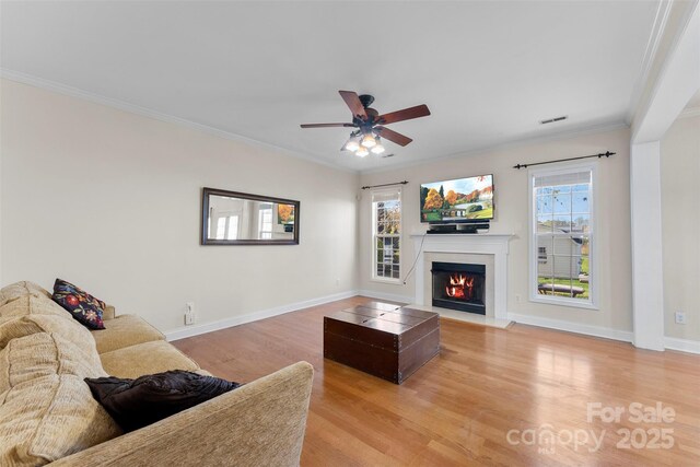 living area with a fireplace with flush hearth, light wood-type flooring, ornamental molding, and baseboards