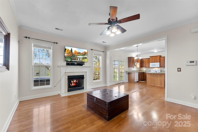 unfurnished living room with visible vents, baseboards, a lit fireplace, ornamental molding, and light wood-type flooring