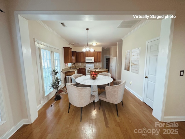 dining area with baseboards, visible vents, ornamental molding, light wood-style floors, and a notable chandelier