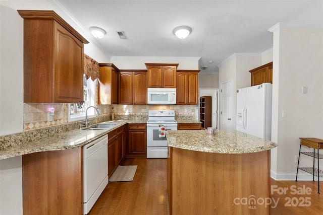 kitchen featuring light stone countertops, white appliances, brown cabinets, and a sink