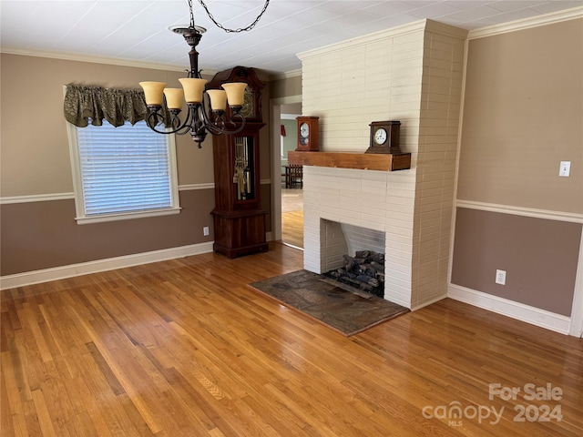 unfurnished living room featuring a brick fireplace, crown molding, wood-type flooring, and a notable chandelier