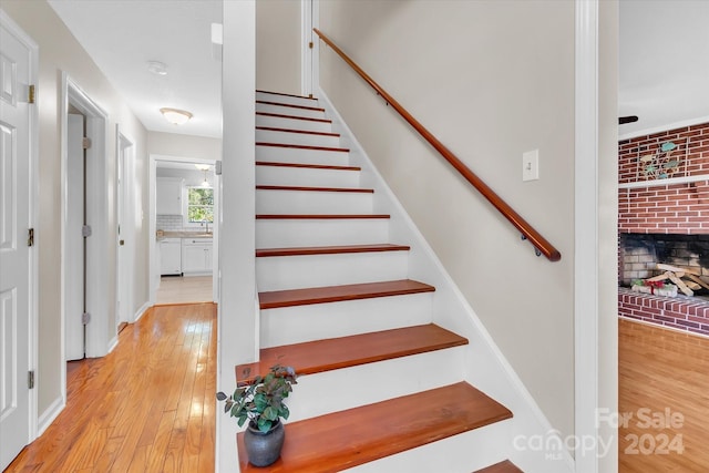 stairway featuring hardwood / wood-style floors and a brick fireplace