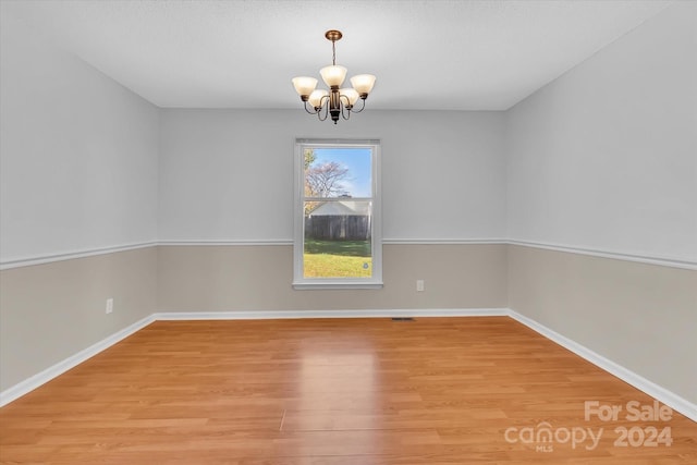 empty room featuring a notable chandelier and light wood-type flooring