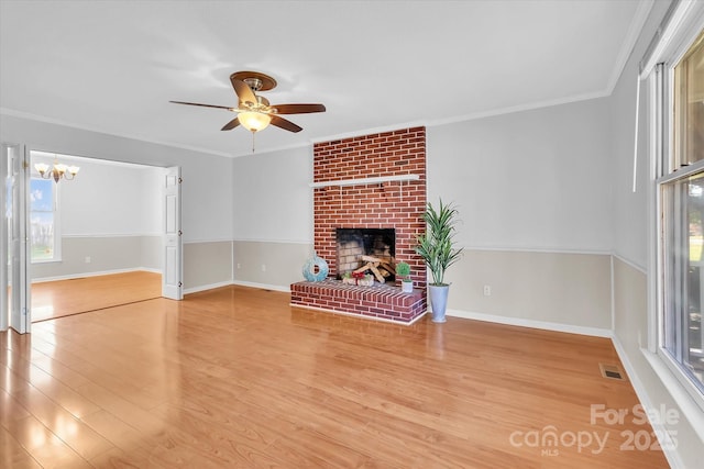 unfurnished living room featuring wood finished floors, ornamental molding, ceiling fan with notable chandelier, a brick fireplace, and visible vents