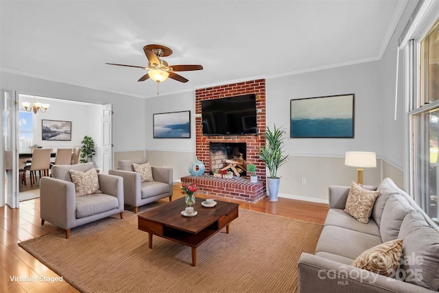 living room featuring ceiling fan with notable chandelier, a fireplace, ornamental molding, wood finished floors, and plenty of natural light
