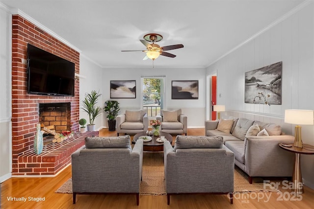 living area featuring crown molding, ceiling fan, wood finished floors, and a fireplace