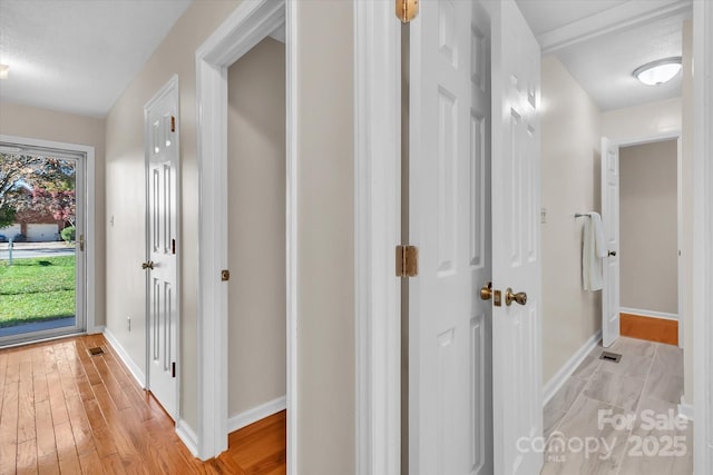 hallway with baseboards, light wood-type flooring, and visible vents