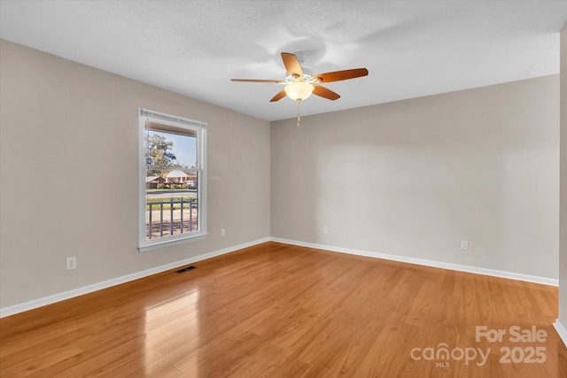 spare room featuring baseboards, visible vents, a ceiling fan, and light wood-style flooring