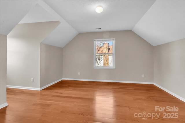additional living space featuring visible vents, baseboards, vaulted ceiling, and light wood-type flooring