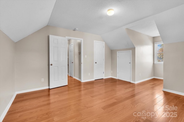 additional living space with light wood finished floors, vaulted ceiling, and baseboards
