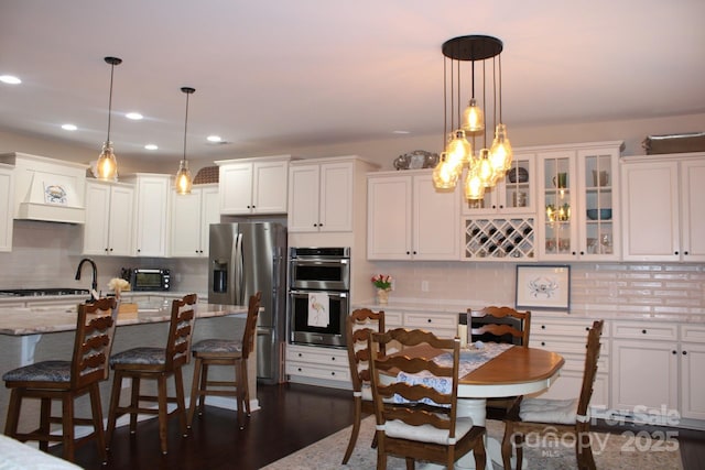 kitchen with stainless steel appliances, white cabinets, hanging light fixtures, and light stone countertops