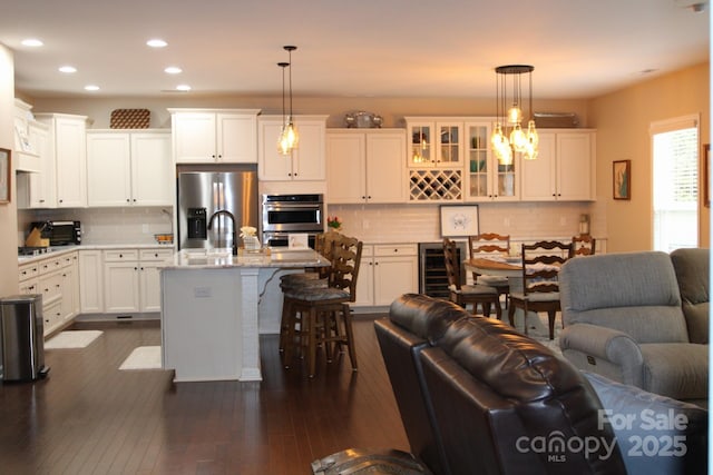 kitchen featuring pendant lighting, white cabinets, wine cooler, stainless steel fridge, and a kitchen island with sink