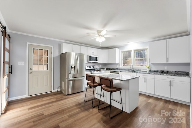 kitchen featuring light wood-type flooring, appliances with stainless steel finishes, a barn door, and a kitchen island