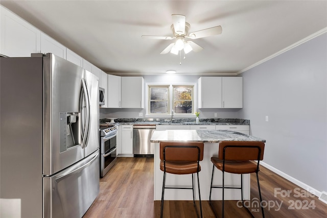 kitchen featuring stainless steel appliances, a kitchen island, light stone counters, light hardwood / wood-style flooring, and white cabinets