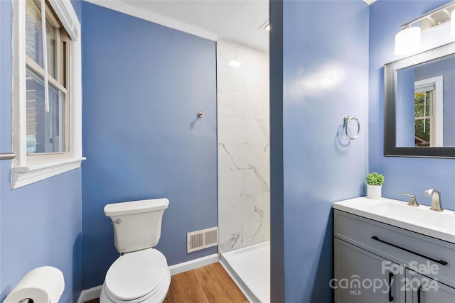 bathroom with a tile shower, vanity, wood-type flooring, and toilet