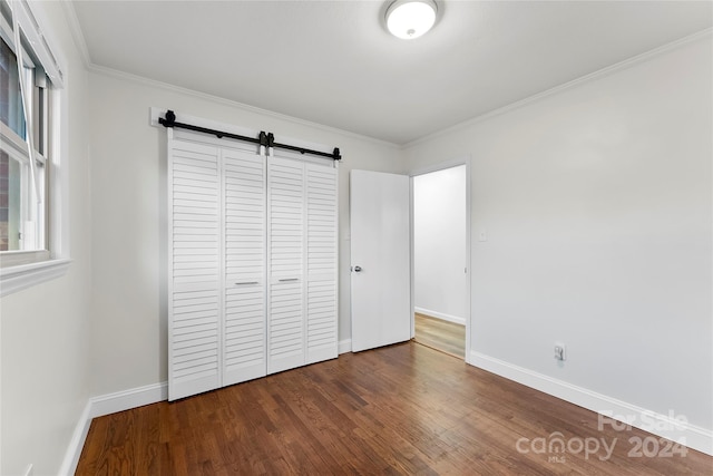 unfurnished bedroom with a barn door, wood-type flooring, ornamental molding, and a closet