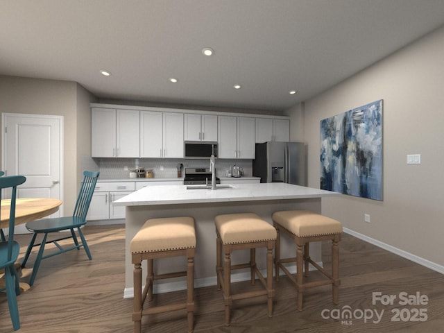 kitchen with a kitchen island with sink, a breakfast bar, white cabinets, appliances with stainless steel finishes, and decorative backsplash