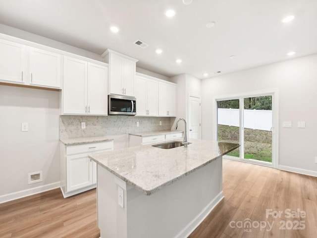 kitchen featuring white cabinets, stainless steel microwave, a sink, and an island with sink