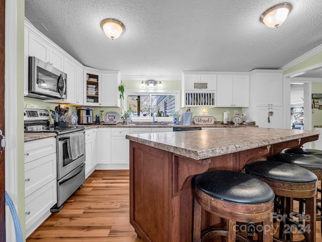 kitchen with a center island, stainless steel appliances, crown molding, a textured ceiling, and light wood-type flooring