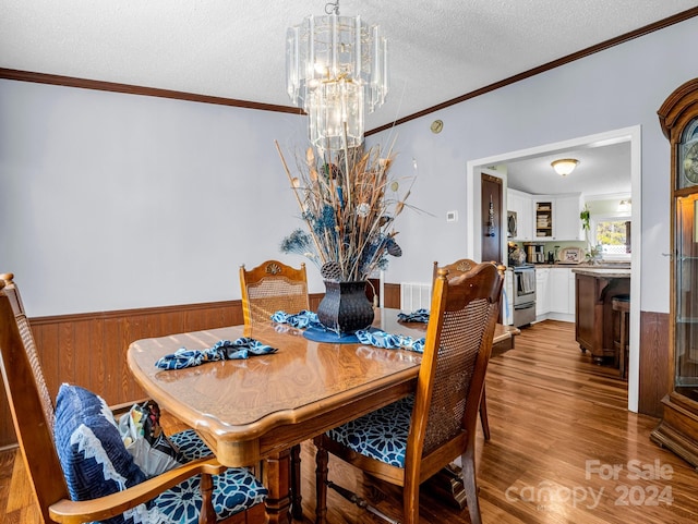 dining space with wood walls, crown molding, a textured ceiling, a notable chandelier, and light hardwood / wood-style floors