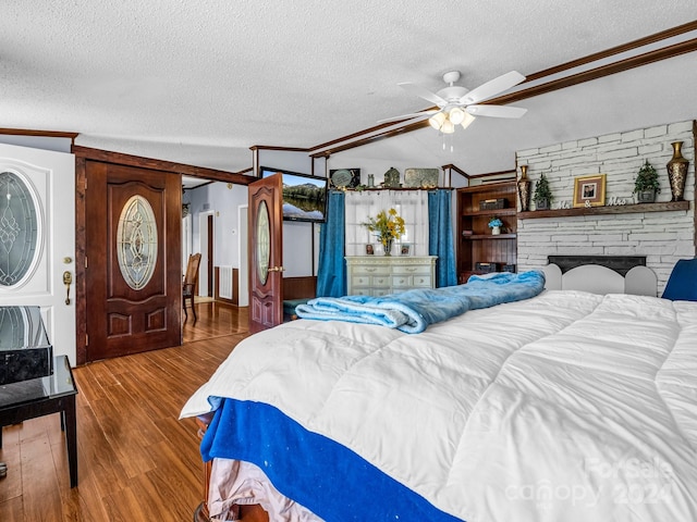 bedroom with ceiling fan, a stone fireplace, lofted ceiling, a textured ceiling, and hardwood / wood-style flooring