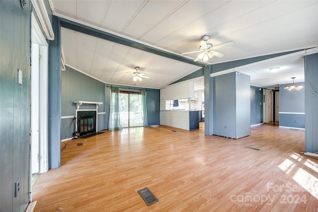 unfurnished living room with wood walls, ceiling fan with notable chandelier, vaulted ceiling, and light wood-type flooring