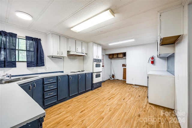 kitchen with light wood-type flooring, blue cabinets, double oven, sink, and white cabinetry