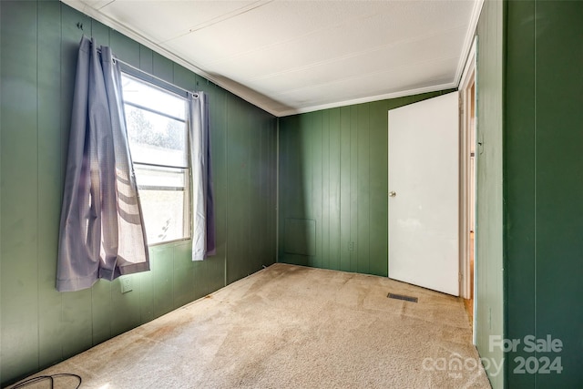 unfurnished room with crown molding, wooden walls, and light colored carpet