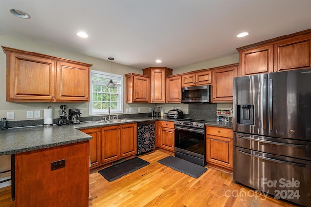 kitchen featuring a breakfast bar, sink, appliances with stainless steel finishes, decorative light fixtures, and light hardwood / wood-style floors