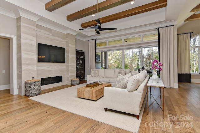 living room featuring a fireplace, beam ceiling, light hardwood / wood-style floors, and ceiling fan