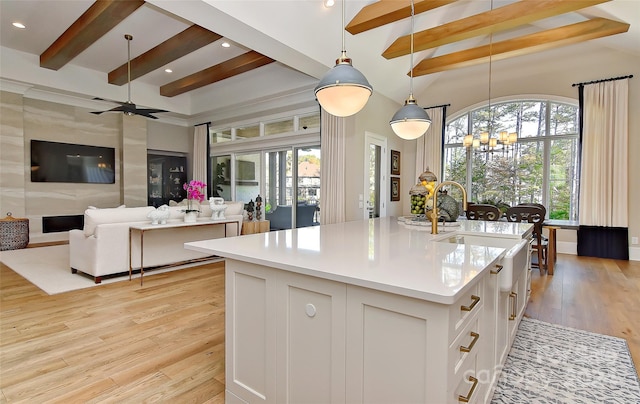 kitchen featuring pendant lighting, light hardwood / wood-style flooring, an island with sink, beam ceiling, and white cabinetry