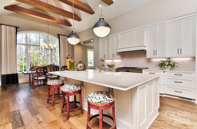 kitchen with backsplash, pendant lighting, white cabinets, light hardwood / wood-style floors, and an island with sink