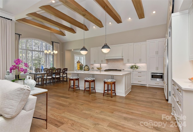 kitchen featuring a kitchen island with sink, light hardwood / wood-style flooring, white cabinets, and decorative light fixtures