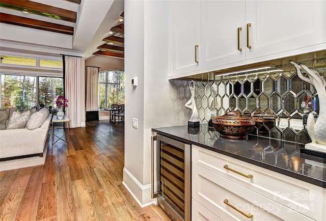 bar with backsplash, white cabinets, beamed ceiling, light hardwood / wood-style floors, and wine cooler