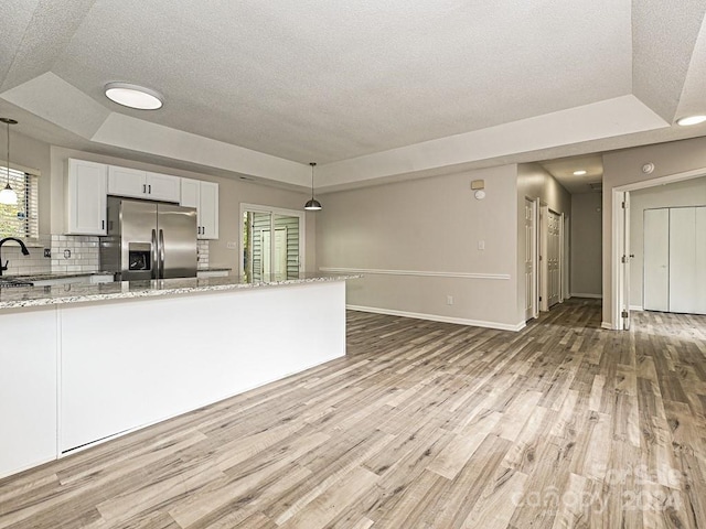 kitchen with a raised ceiling, stainless steel fridge with ice dispenser, decorative light fixtures, light stone counters, and white cabinetry