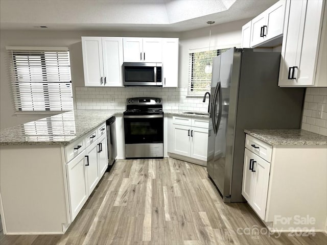 kitchen with kitchen peninsula, light stone countertops, white cabinets, and appliances with stainless steel finishes