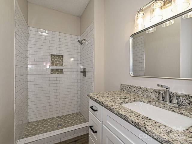 bathroom with a tile shower, vanity, a textured ceiling, and hardwood / wood-style floors