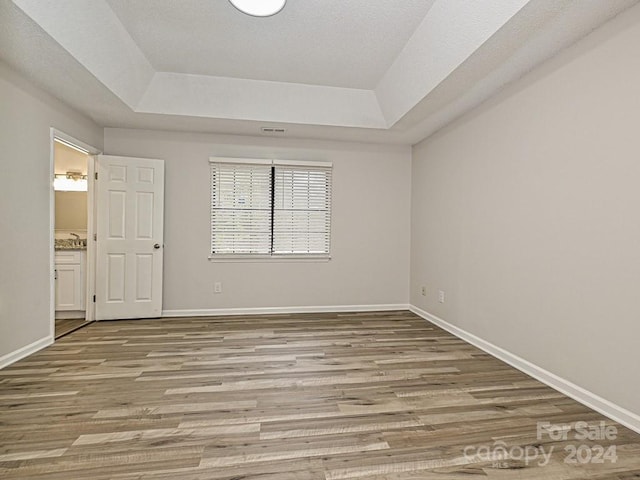 empty room with light wood-type flooring and a tray ceiling