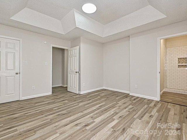 unfurnished bedroom featuring wood-type flooring, connected bathroom, and a tray ceiling