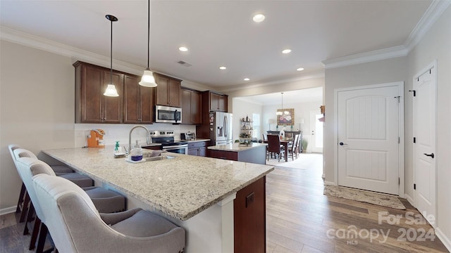 kitchen with sink, light hardwood / wood-style flooring, decorative light fixtures, kitchen peninsula, and stainless steel appliances