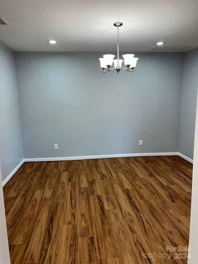 spare room with hardwood / wood-style floors and an inviting chandelier