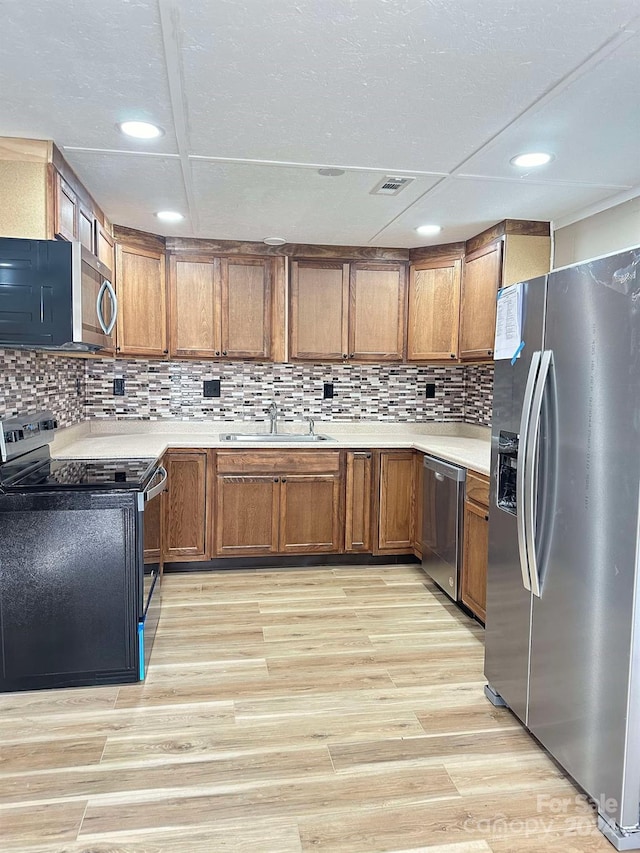 kitchen featuring stainless steel appliances, light hardwood / wood-style flooring, tasteful backsplash, and sink