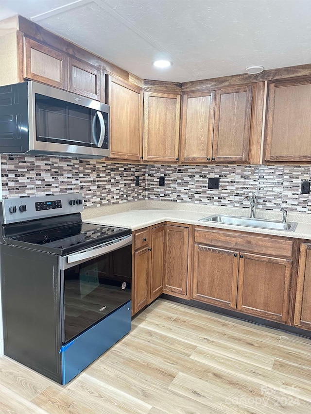 kitchen featuring backsplash, sink, light wood-type flooring, and appliances with stainless steel finishes